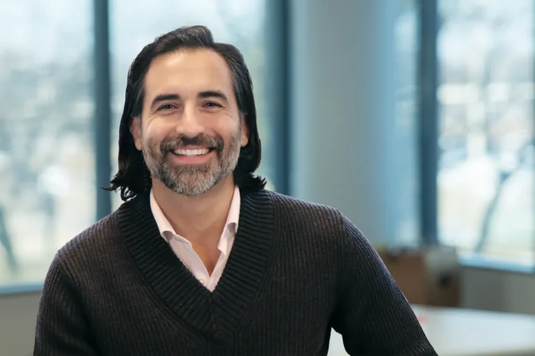 Smiling man with shoulder-length dark hair and salt-and-pepper beard in office setting