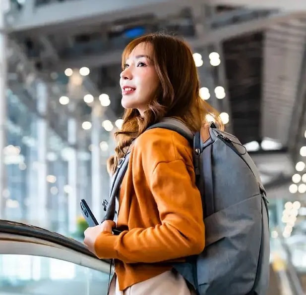 Young woman with gray backpack on escalator in bright modern airport terminal