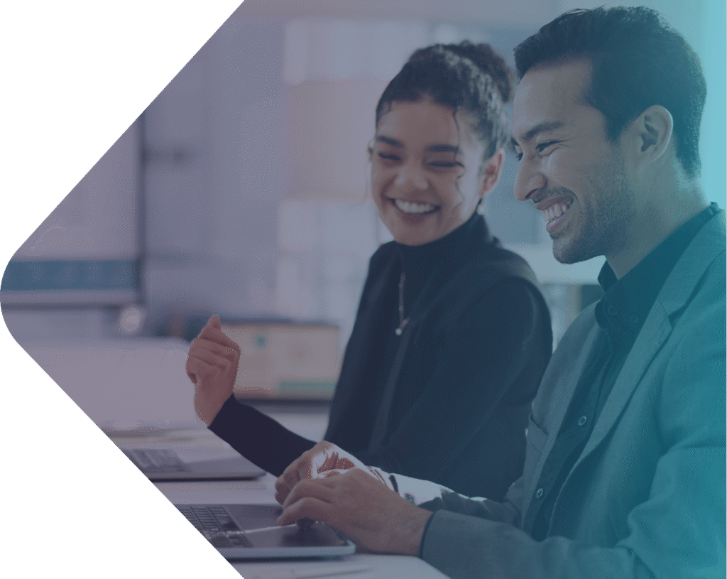 Two coworkers smiling and working together on laptops in a modern office